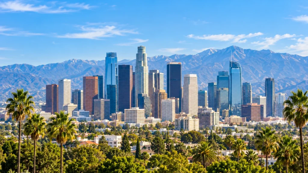 Downtown skyline of glass towers in front of a mountain range, framed by palm trees under a blue sky