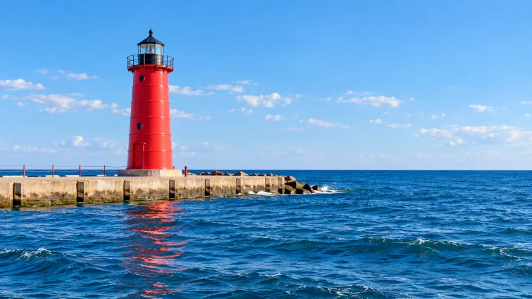 Red pier lighthouse at the end of a concrete breakwater, with deep blue water and a clear sky
