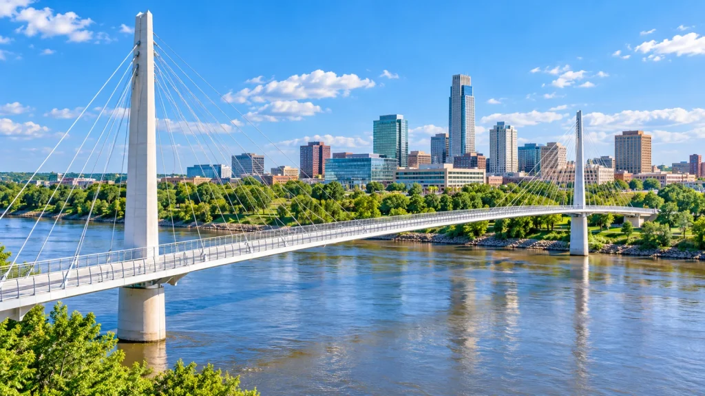 White cable-stayed pedestrian bridge over a wide river in front of a downtown skyline